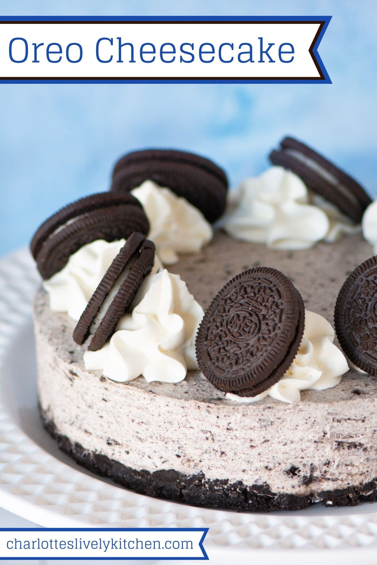 A no-bake Oreo cheesecake topped with swirls of whipped cream and Oreos, on a white cake stand.