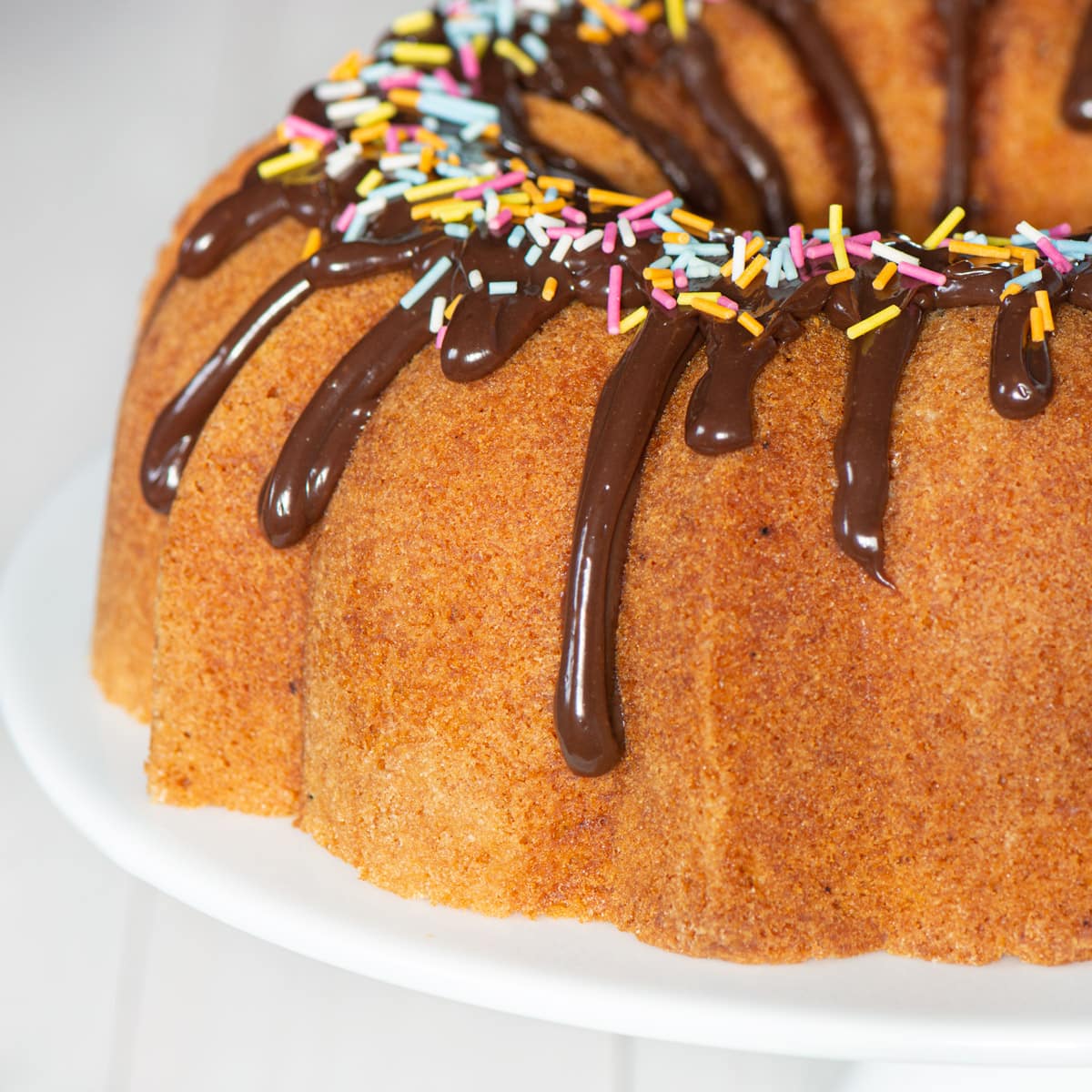 Vanilla bundt cake topped with milk chocolate ganache and sprinkles.