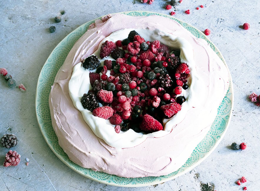 Pink vegan pavlova topped with whipped coconut cream and berries.