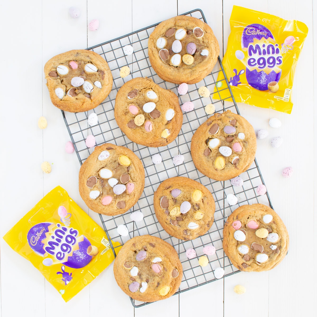 Mini egg cookies on a cooling rack with packets of mini eggs. 