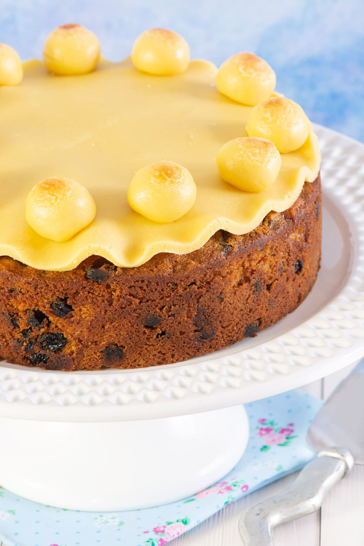 Close up of decorated simnel cake on a white cake stand. 