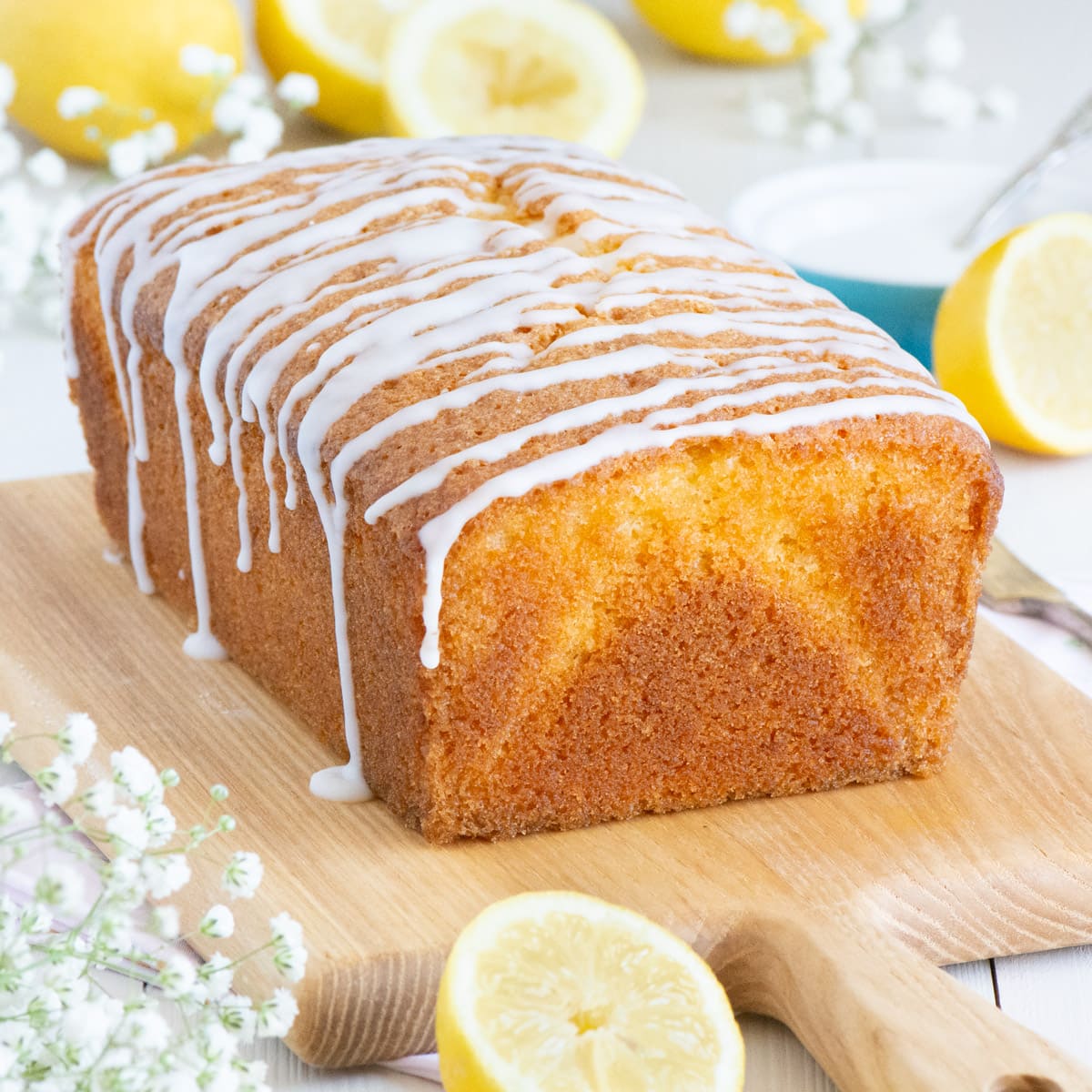 Unsliced lemon loaf cake viewed at eye level with the lemon icing drip visible. 