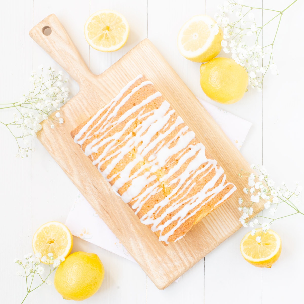 Unsliced lemon drizzle cake as seen from above on a wooden board. 